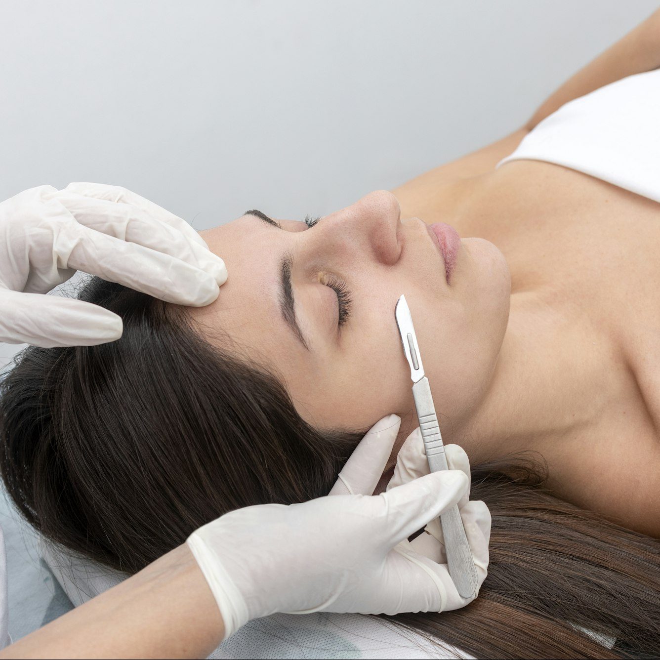 Closeup of the doctor with a scalpel treating the woman's skin. Dermaplaning treatment.