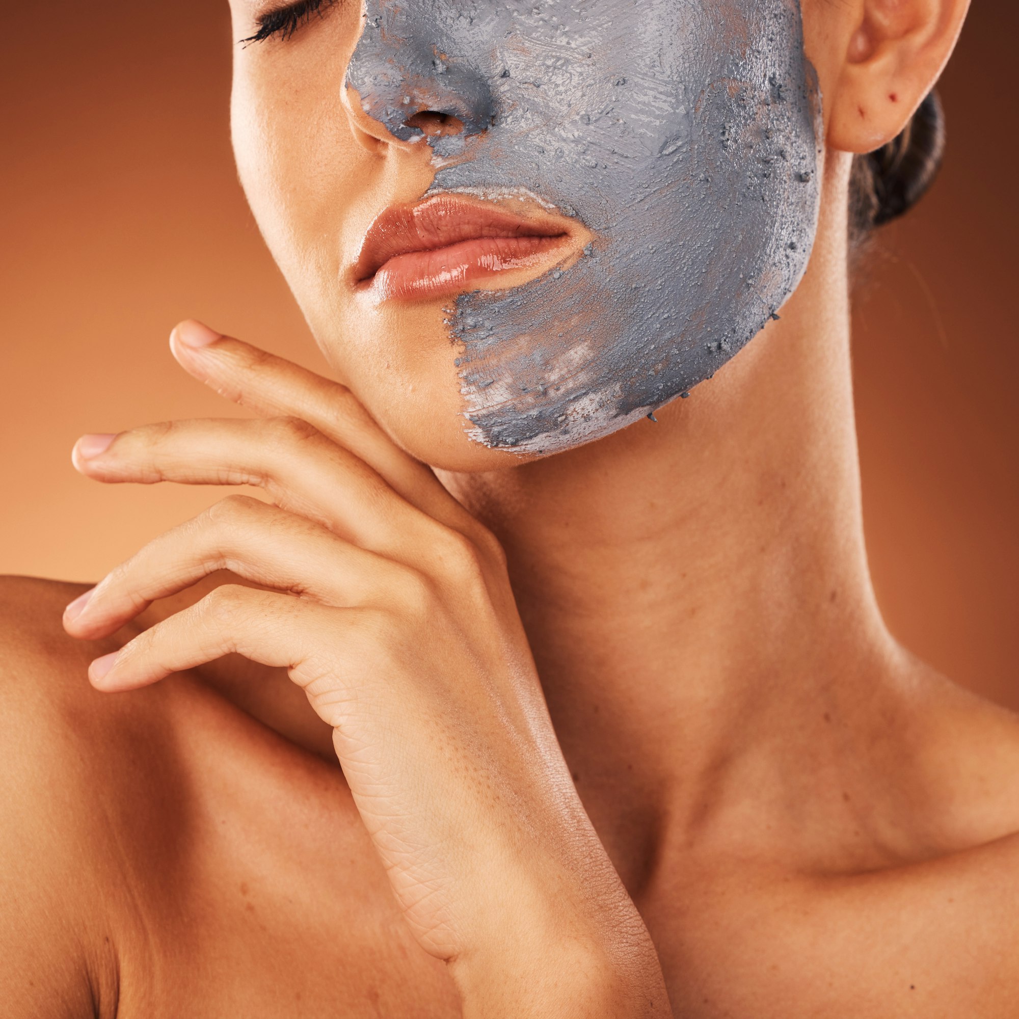 Woman, face mask or skincare mud facial on orange studio background in self care, dermatology or ac